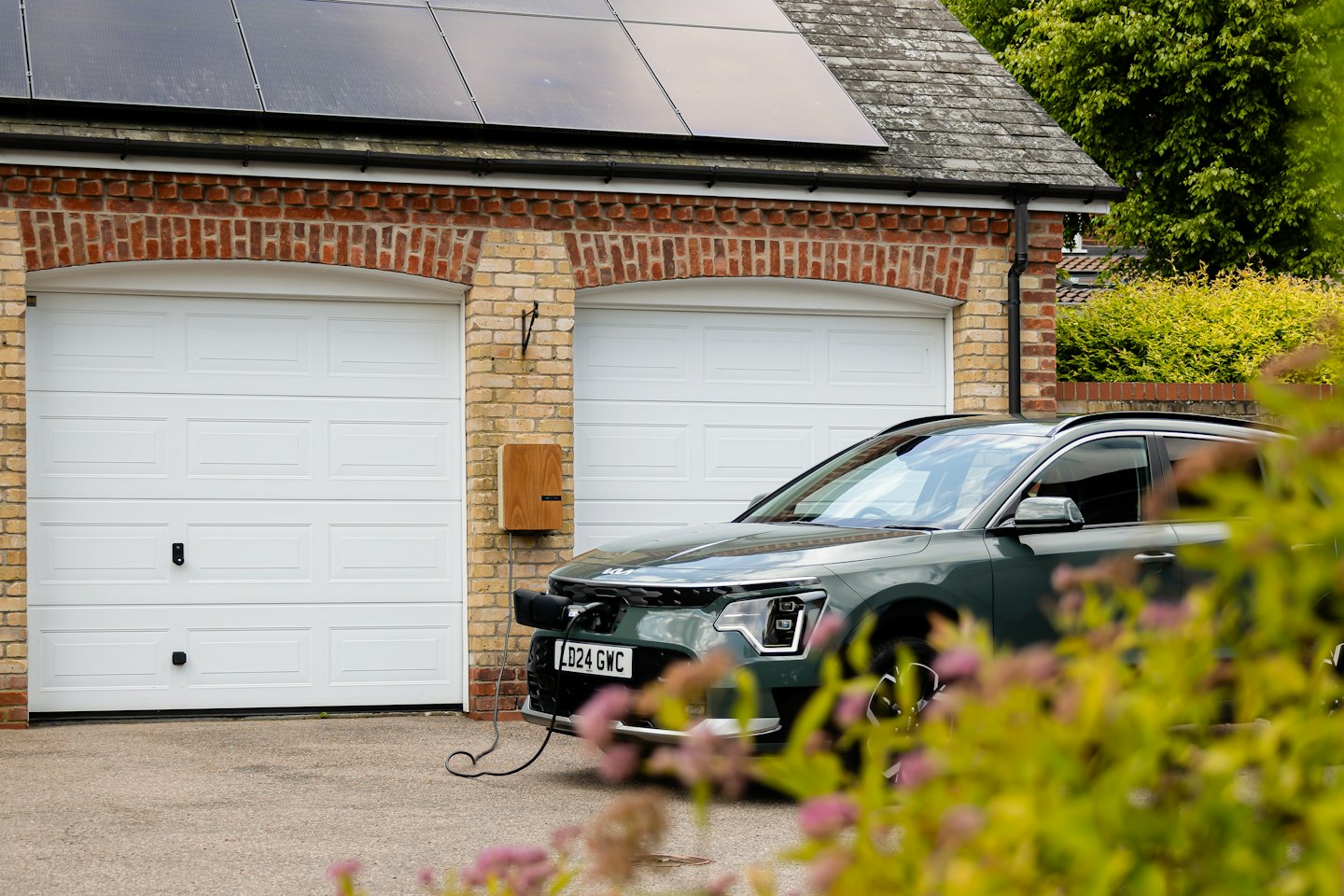 Coche eléctrico verde oscuro enchufado a un punto de carga doméstico.